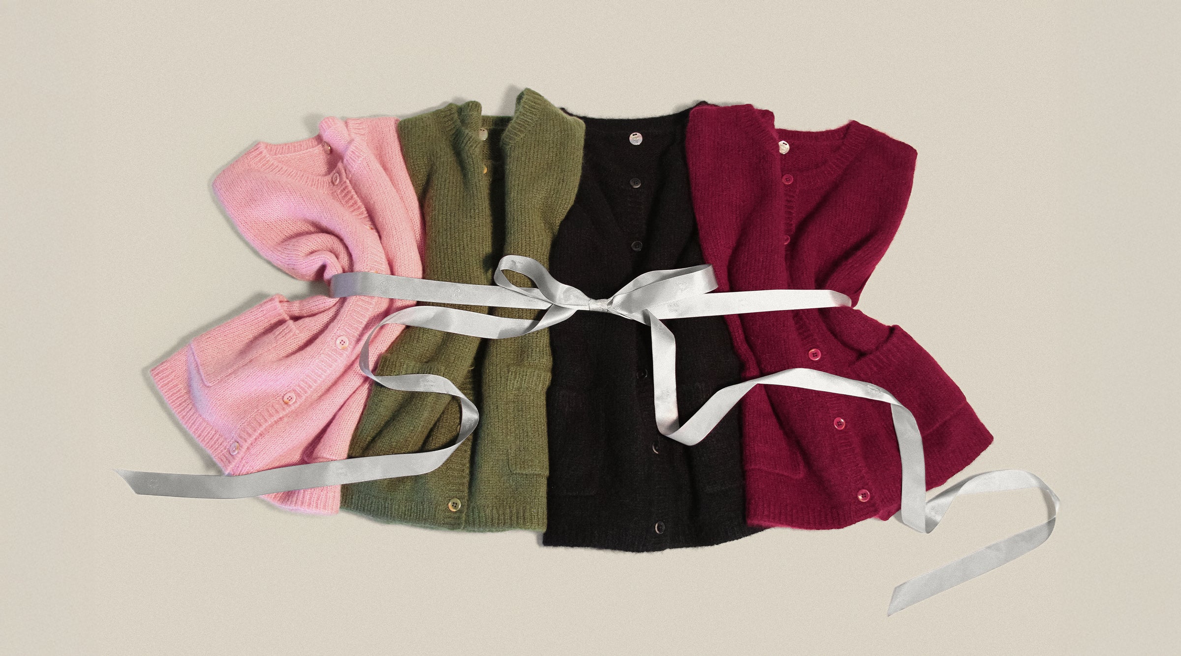 Four colorful coco cardigans by Margaret O'Leary tied together with a white ribbon on a beige background