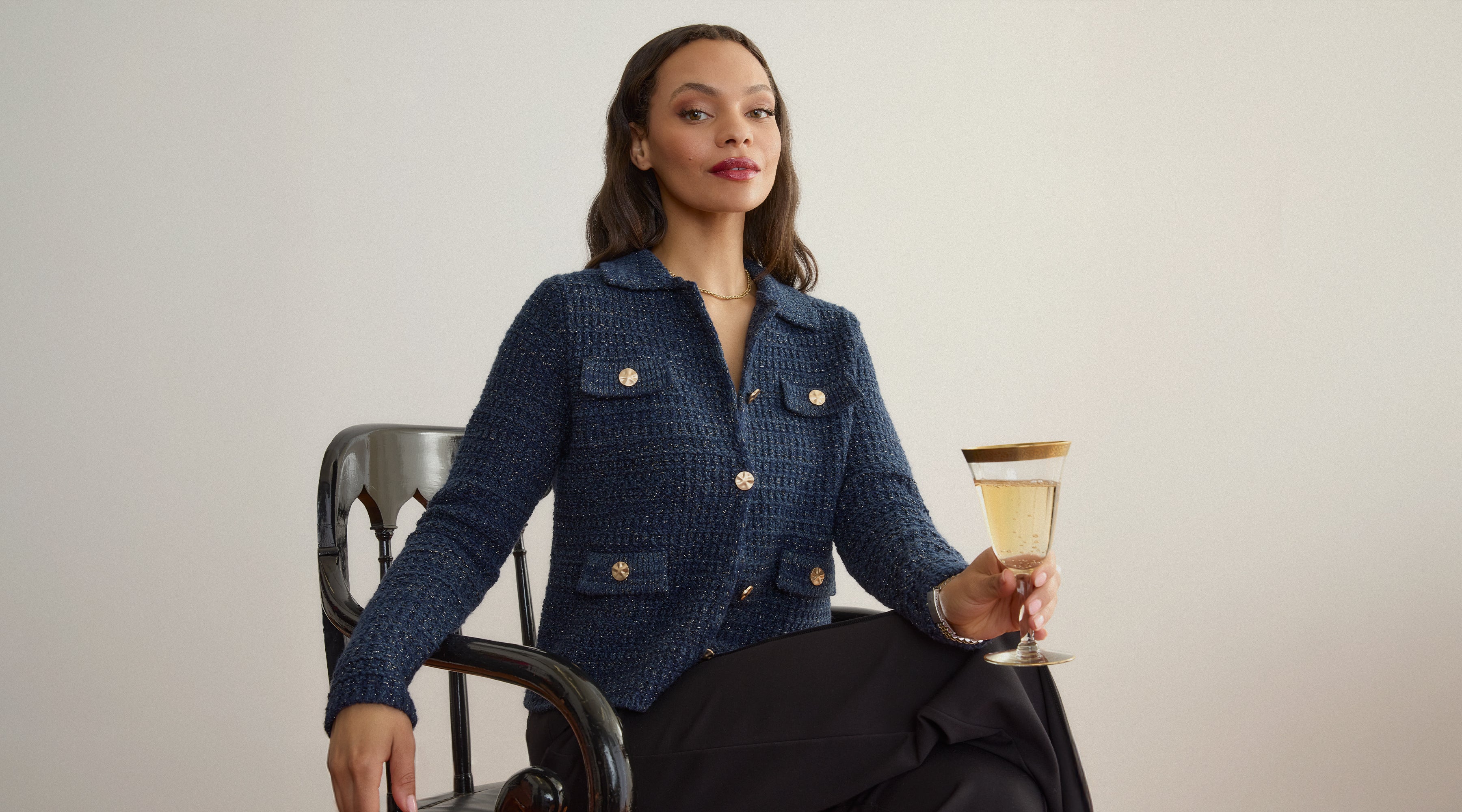 Woman in a blue textured Gabriella jacket by Margaret O'Leary holding a cocktail glass against a plain background