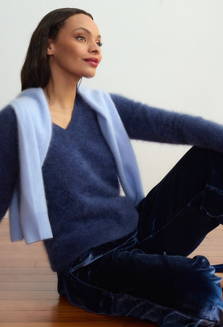 Woman wearing a blue sweater and light blue cardigan sitting on a wooden floor.