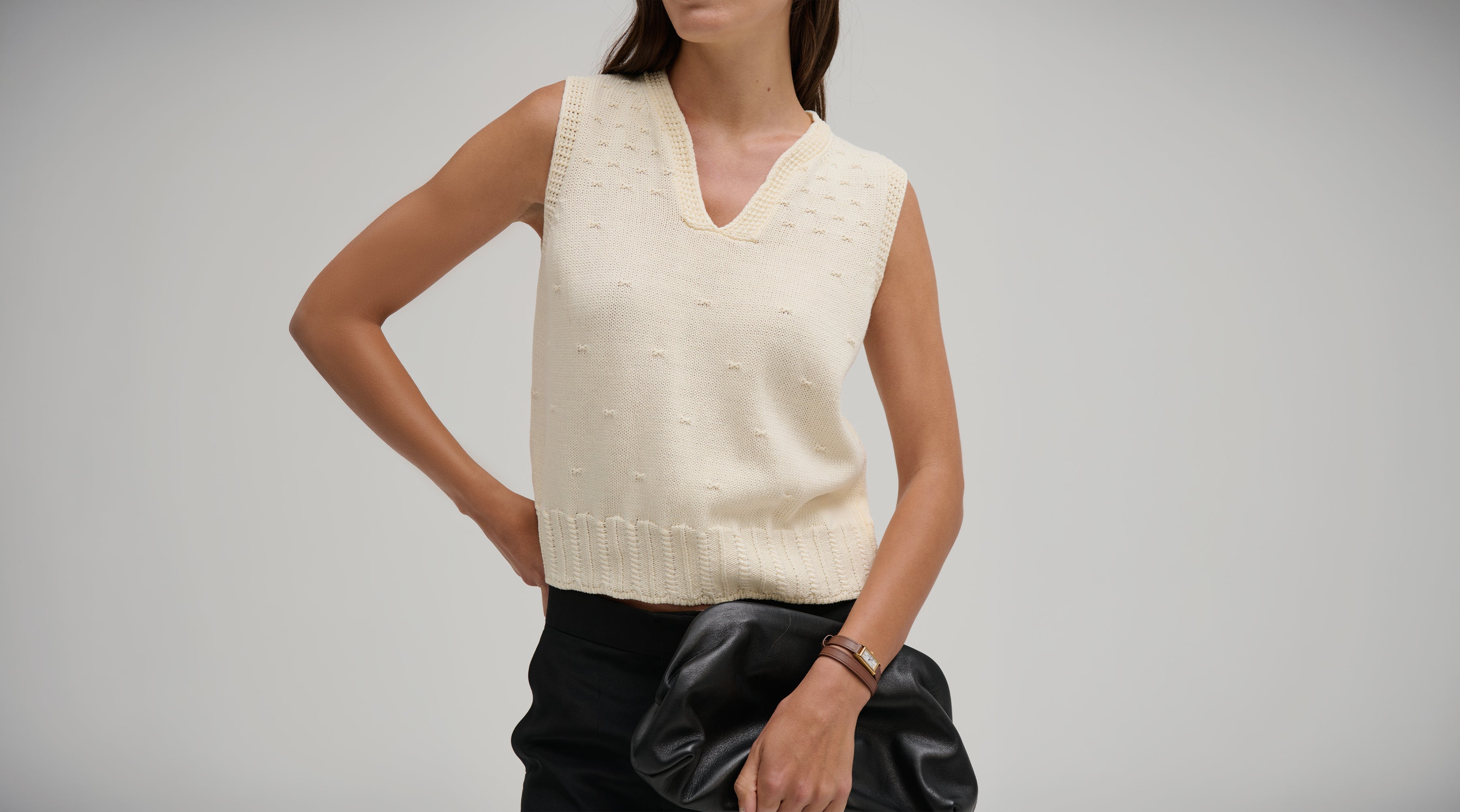 Woman wearing a cream sleeveless Nina Split Neck Tank by Margaret O'Leary against a gray background