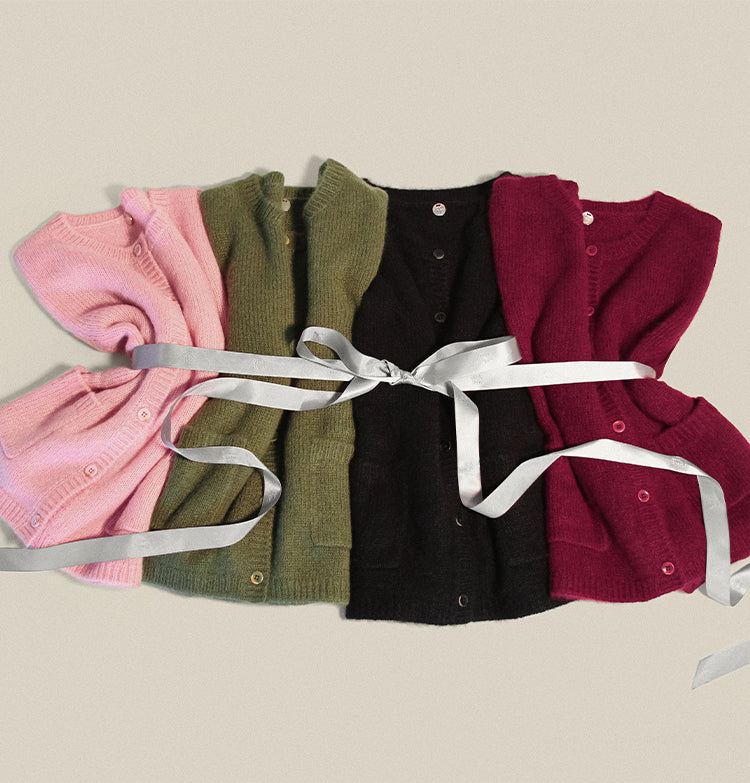 Four colorful coco cardigans by Margaret O'Leary tied together with a white ribbon on a beige background