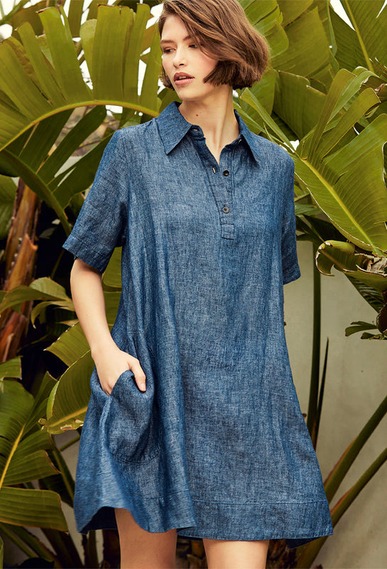 Woman wearing the Voluminous Shirt Dress in Indigo by Margaret O'Leary in front of a palm leaf background.