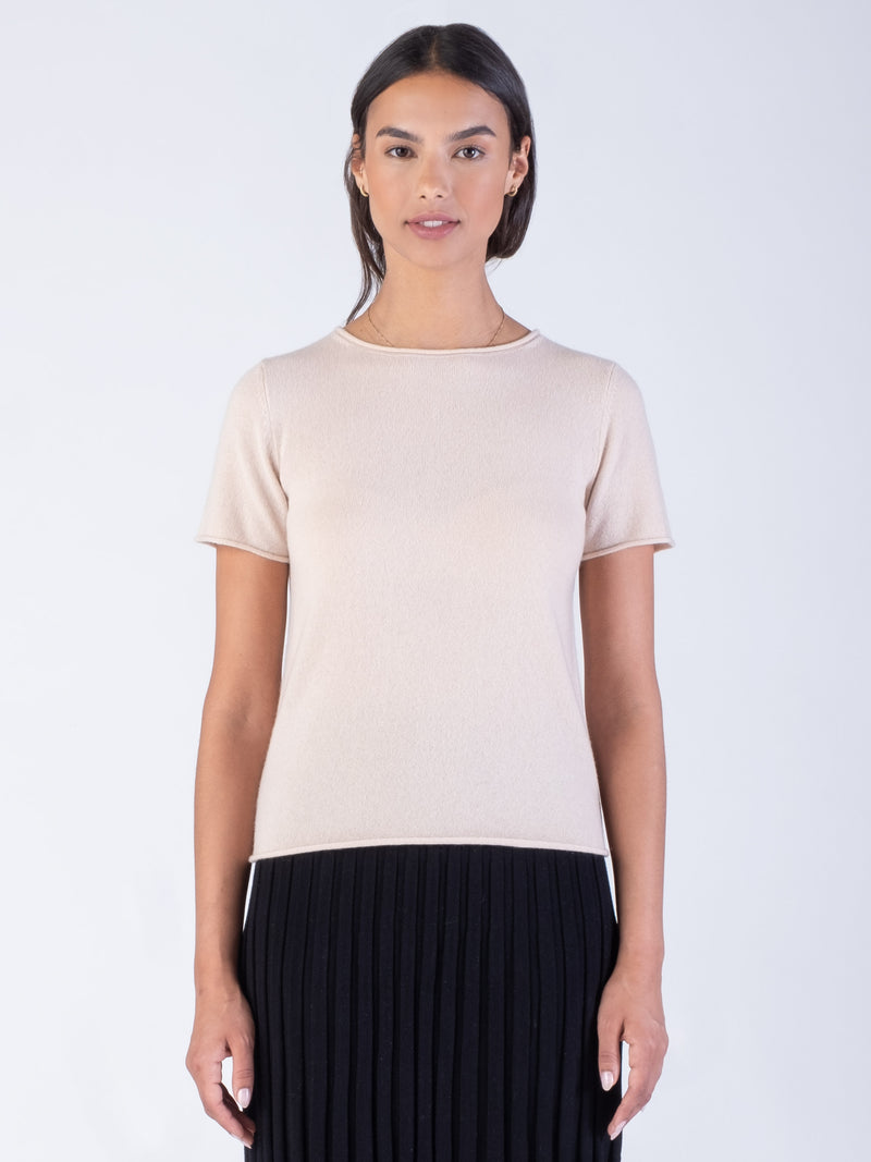 Model wearing a light pinkish beige cashmere tee and a black pleated skirt.