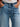 Person wearing a white knit top and  jeans with a navy belt by Margaret O'Leary on a white background