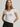 Woman wearing a white Stretch Scoop Tee and grey pants by Margaret O'Leary against a plain background