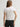Woman wearing a white Stretch Scoop Tee and grey pants by Margaret O'Leary against a plain background
