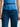 Person wearing a blue top and dark jeans with a black belt by Margaret O'Leary on a white background