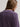A close-up back view of a woman wearing a textured, fuzzy purple knit sweater against a plain light gray background.