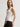 Woman wearing a white Stretch Scoop Tank and grey pants by Margaret O'Leary against a plain background