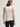 Woman wearing a white Stretch Scoop Tank and grey pants by Margaret O'Leary against a plain background