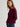 A woman wearing a cashmere coco cardigan in deep burgundy with front buttons and patch pockets by Margaret O'Leary, paired with blue jeans, photographed against a plain light gray studio background.