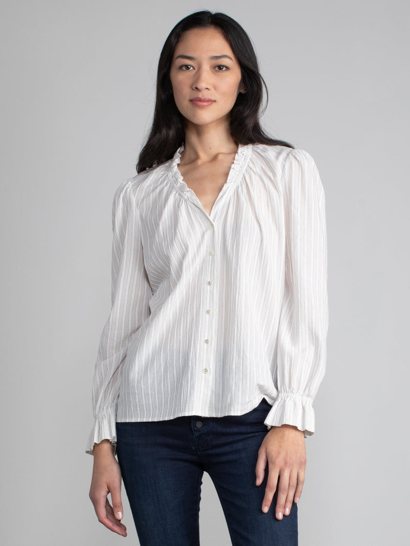 Female model wearing white blouse with ruffled neckline and cuffs. 