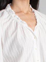 Female model wearing white blouse with ruffled neckline and cuffs. 