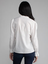 Female model wearing white blouse with ruffled neckline and cuffs. 