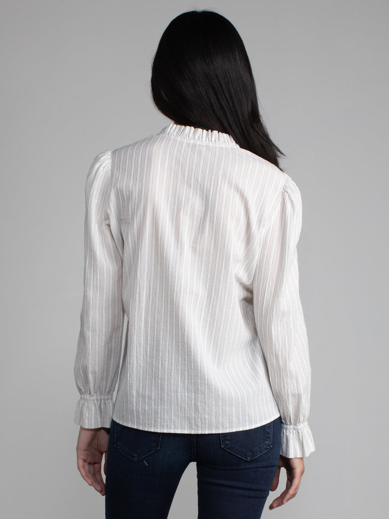 Female model wearing white blouse with ruffled neckline and cuffs. 