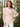 A woman wearing a light peach and white vertically striped long-sleeve button-up shirt, standing in front of a blurred background of green bamboo trees.