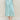 Woman wearing a turquoise satin cinched Clementine Skirt and matching boucle Colette Crew Cardigan by Margaret O'Leary.