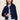 Person wearing a dark blue denim Alma Jacket by Margaret O'Leary with silver buttons and white pants on a beige background