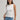 Woman wearing a white sleeveless pima tank top by Margaret O'Leary and blue jeans against a plain background