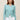 Woman wearing a aqua colored boucle Colette Crew Cardigan by Margaret O'Leary with white pants
