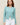 Woman wearing a aqua colored boucle Colette Crew Cardigan by Margaret O'Leary with white pants