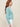 Woman wearing a aqua colored boucle Colette Crew Cardigan by Margaret O'Leary with white pants