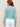 Woman wearing a aqua colored boucle Colette Crew Cardigan by Margaret O'Leary with white pants