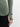 Close-up of a person wearing a sage green waffle-knit long-sleeve top with thumbholes and black pants, against a light gray background.