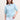 Woman wearing a light blue Z-Stitch Polo by Margaret O'Leary with white pants on a beige background