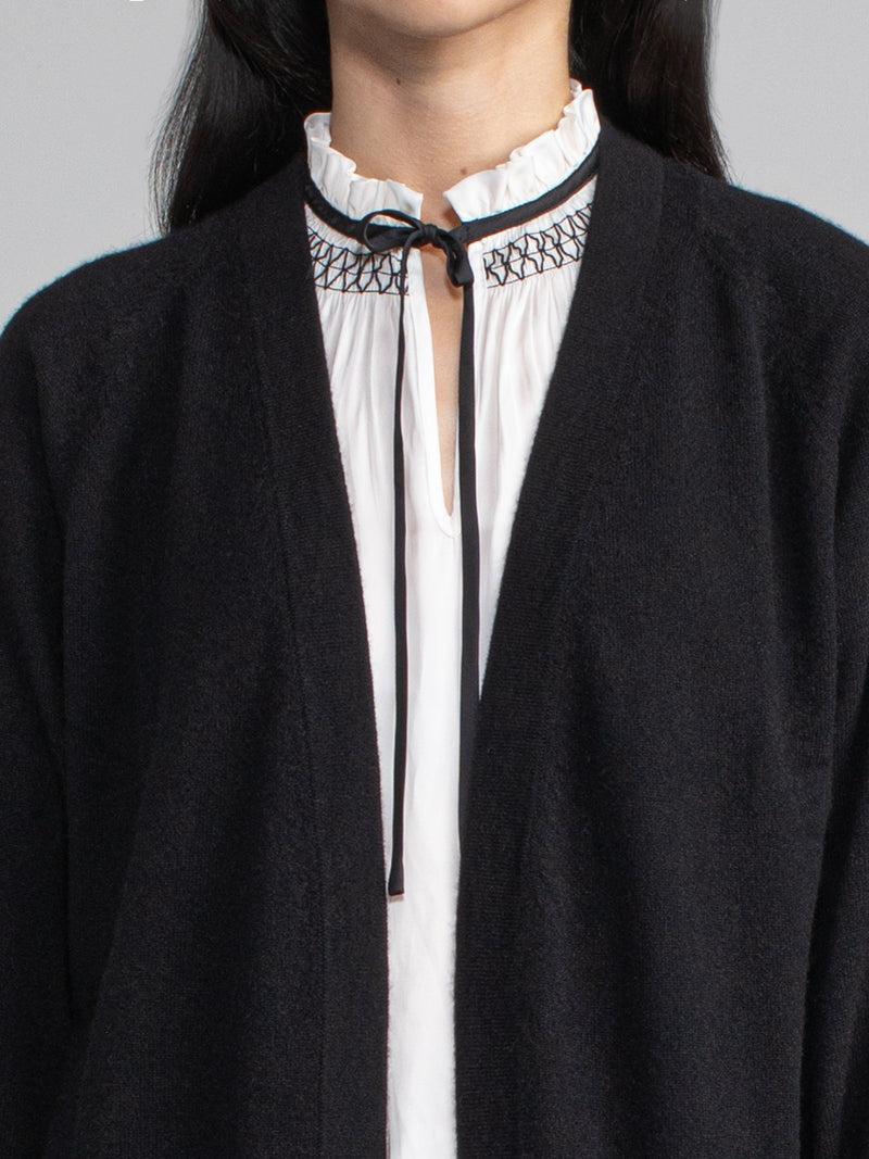 Close up of woman wearing a black cashmere duster over a white and black tie neck top.