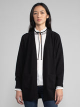 Woman wearing a black cashmere duster over a white and black tie neck top.