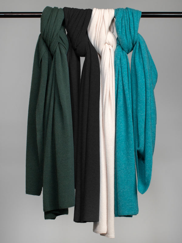 A green, black, off-white, and teal cashmere wraps hangin on a metal bar. 