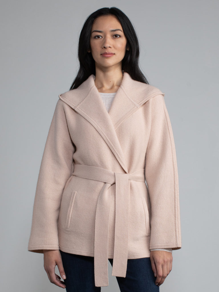 Female model wearing a light pink hooded jacket with a belt.