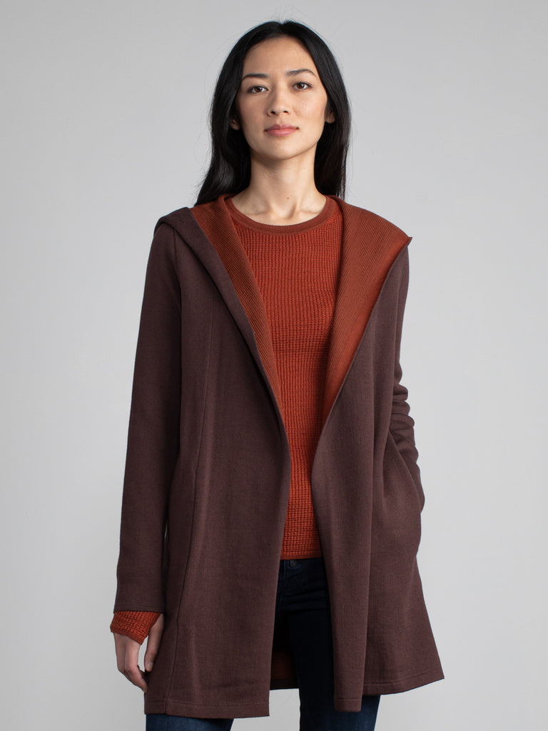 Woman in a maroon and red, long line hooded cardigan.