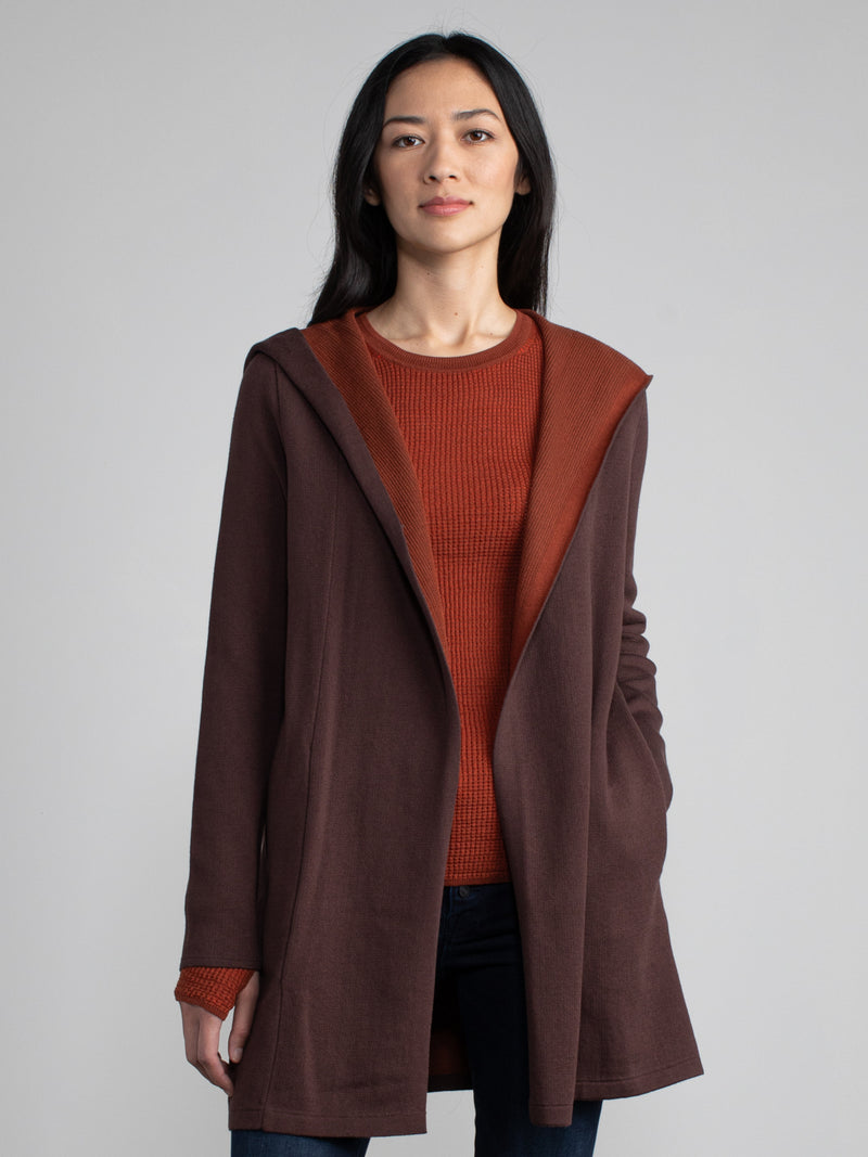 Woman in a maroon and red, long line hooded cardigan.