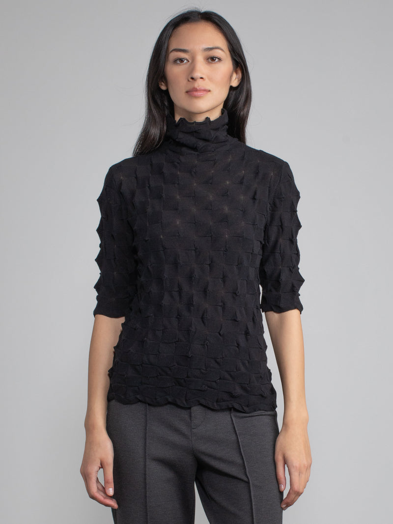 Model wearing the black elbow tneck and a pair of pants.