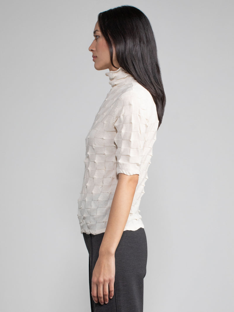 Side view of the model wearing the eggshell elbow tneck and a pair of pants.