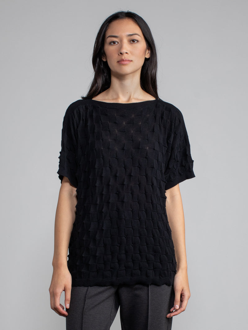 Model wearing the pullover in black and a pair of grey pants.