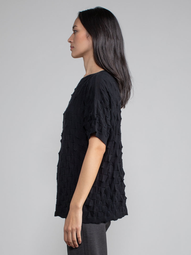 Side view of the model wearing the pullover in black and a pair of grey pants.