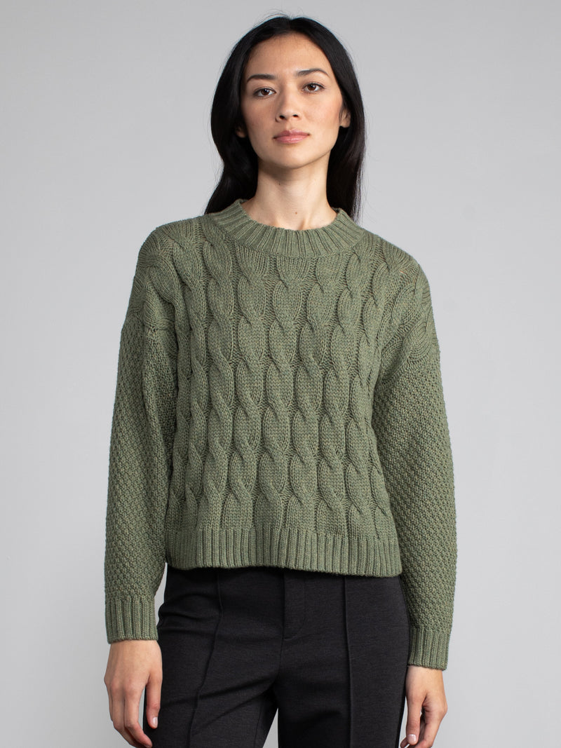 Woman wearing a cropped green cable knit sweater.