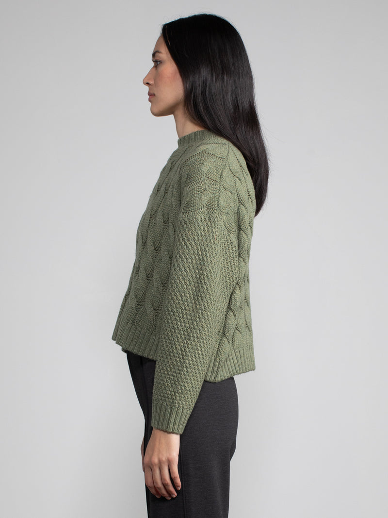 Woman wearing a cropped green cable knit sweater.