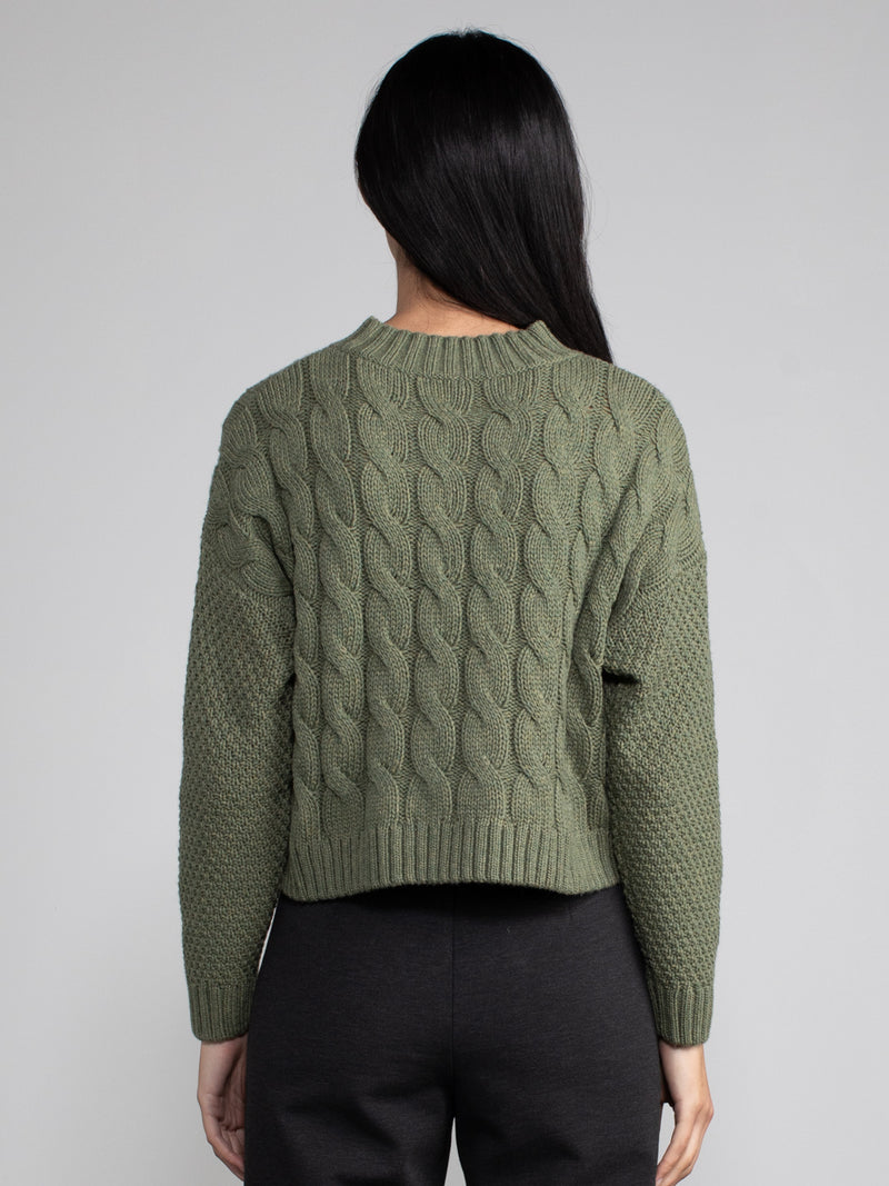 Woman wearing a cropped green cable knit sweater.