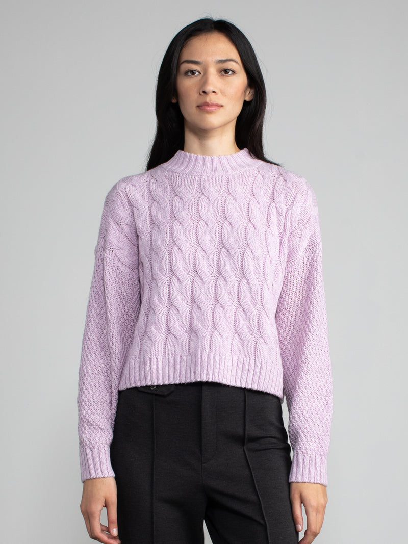 Woman wearing a cropped purple cable knit sweater.