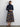 Woman wearing a navy turtleneck and plaid skirt against a white wall