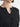Person wearing a black cardigan with gold buttons and a gold necklace on a plain background