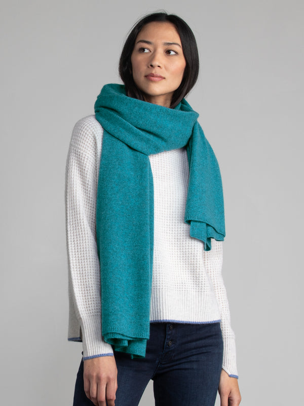 Woman wearing a light grey sweater and teal cashmere wrap.