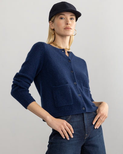 Woman wearing Coco Cardigan in navy made by Margaret O'Leary with jeans and a black hat.