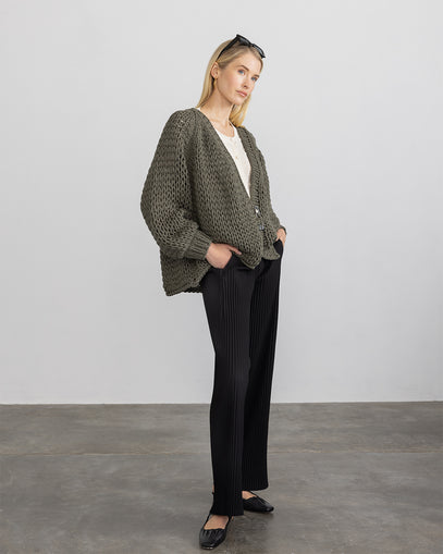 Woman wearing Handknit Cardigan in Olive, the Dimensional Cardi in ivory, and the Pleated Pull on Pant in black made by Margaret O'Leary.