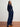 Woman wearing a navy velvet outfit standing on a wooden floor with a white wall background
