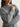 Gray sweater with snowflake patterns worn by a person on a plain background